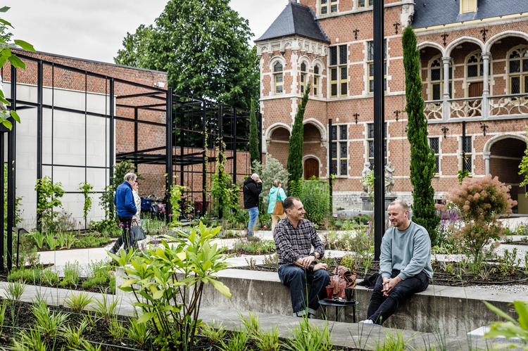 Verschillende duo's mensen lopen en zitten in de museumtuin. Er zijn verschillende soorten planten te zien.